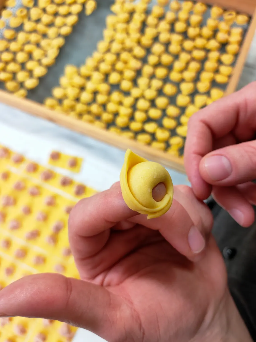 Un tortellino chiuso a mano, con altri tortellini sullo sfondo